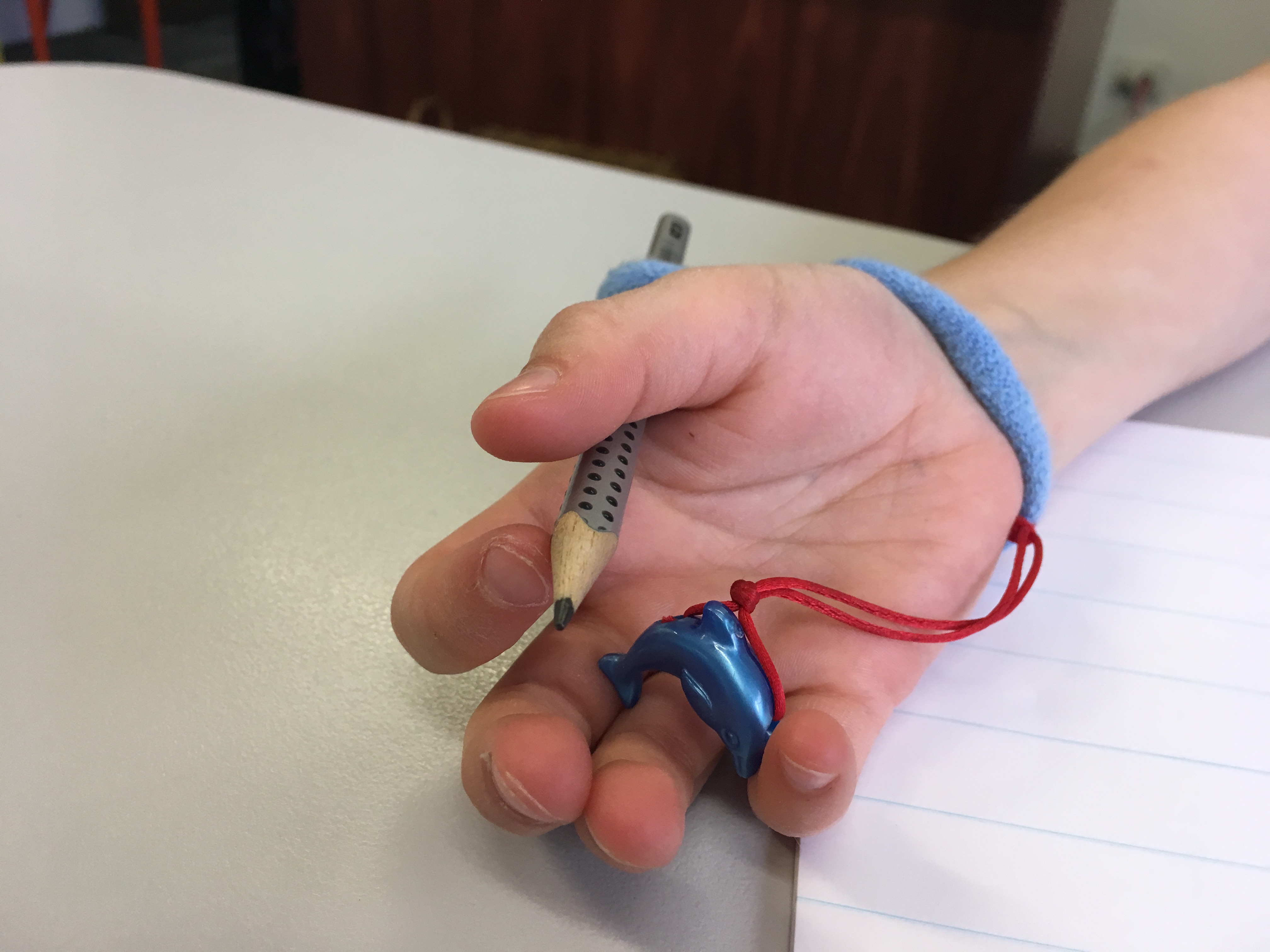 Pencil grip with string attached, showing device in hand