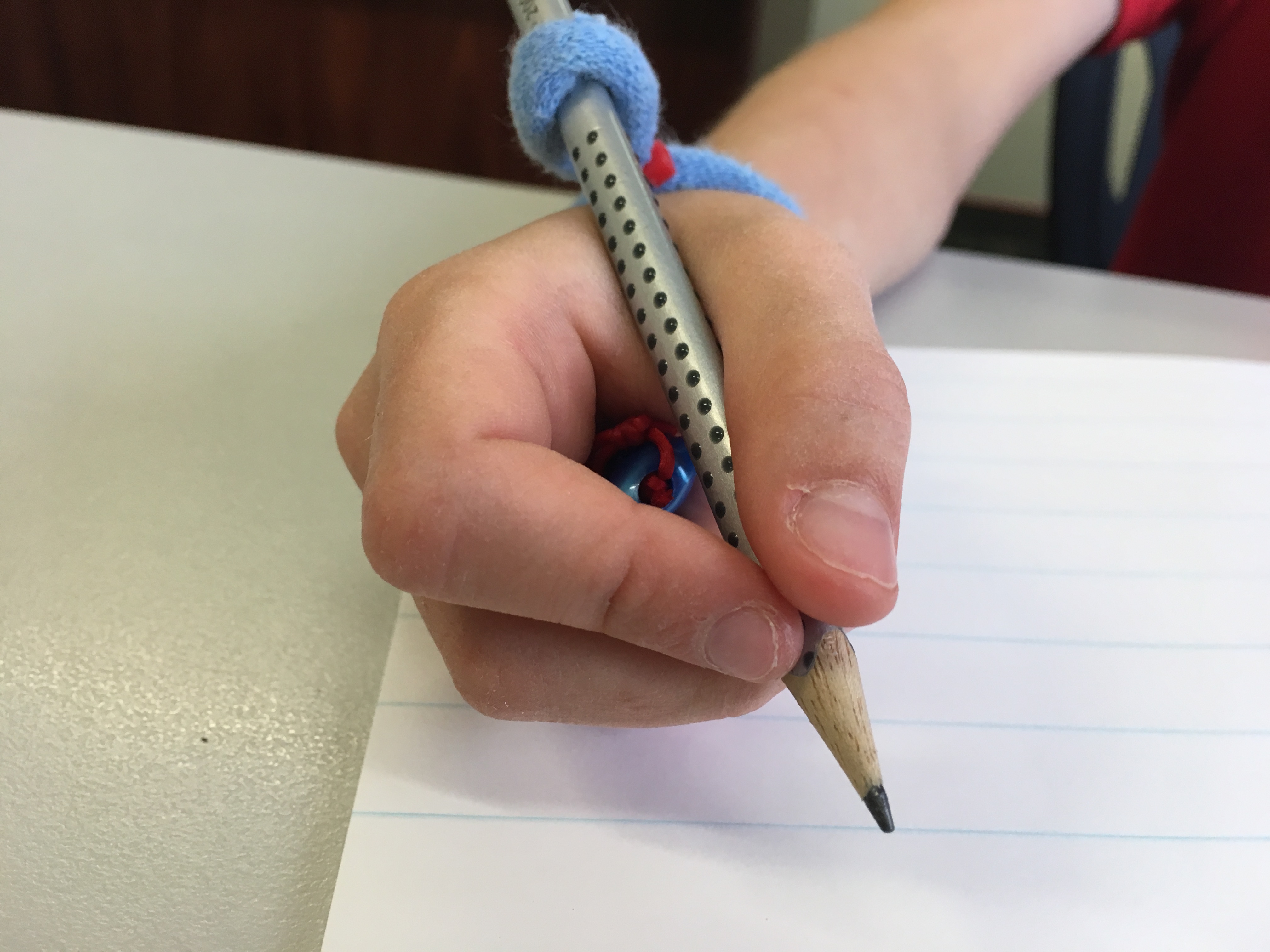 Pencil grip with string attached, showing device in hand, writing